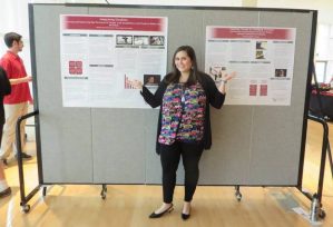 Photo of Davi standing in front of a large bulletin board with two posters.